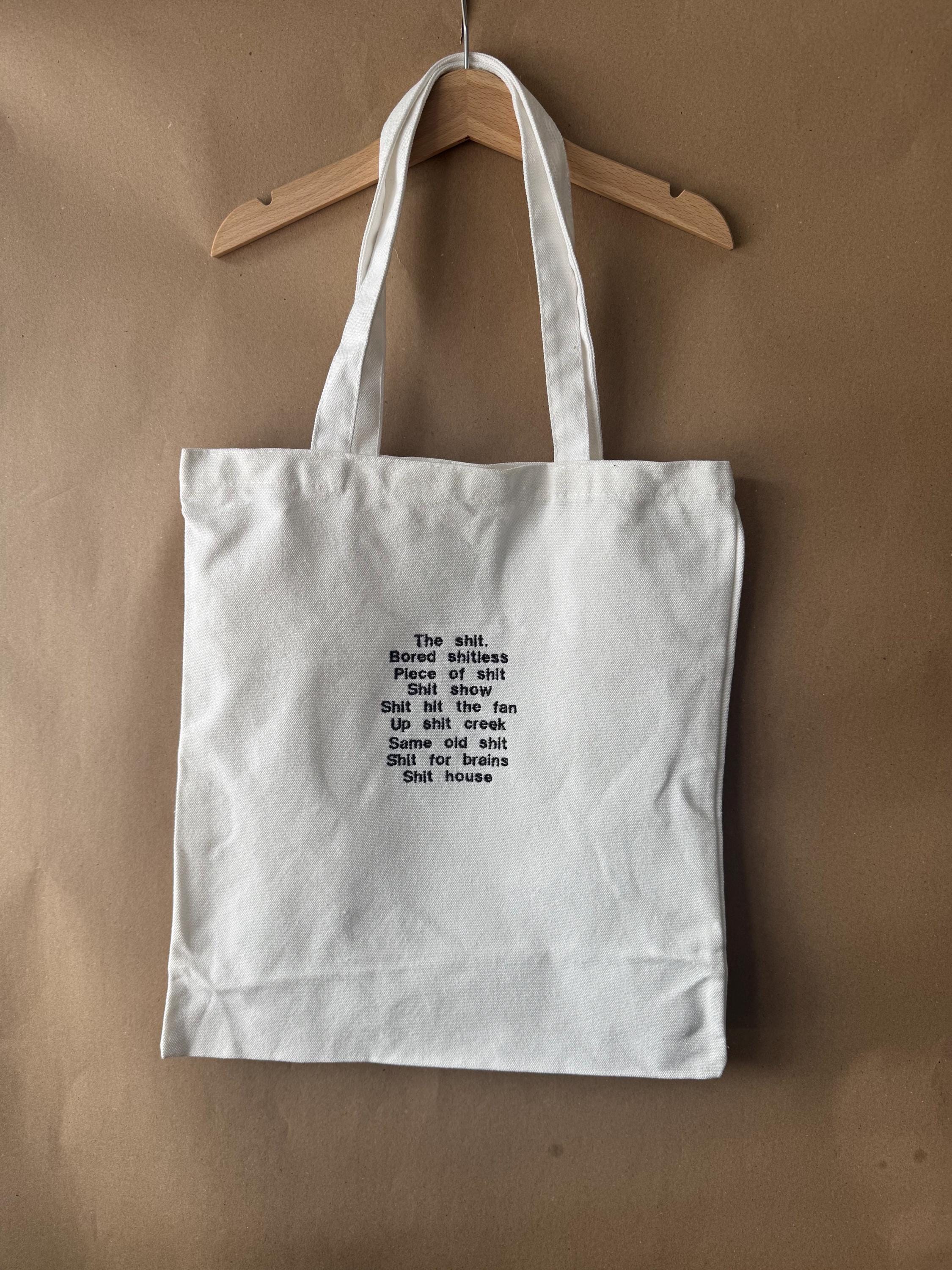 White tote bag with shit uk slang quotes embroidered in brown.