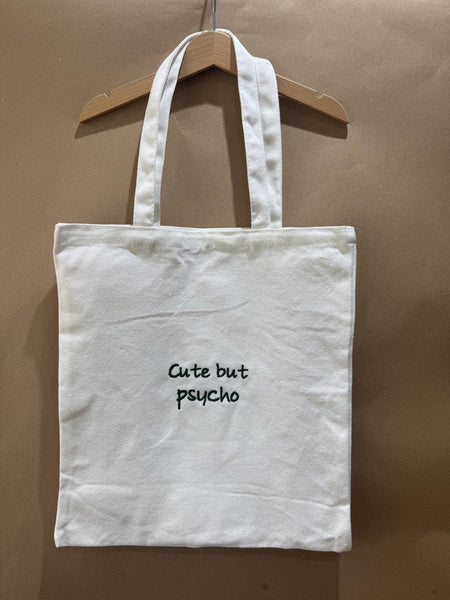 White tote bag with ‘cute but psycho’ embroidered in green.