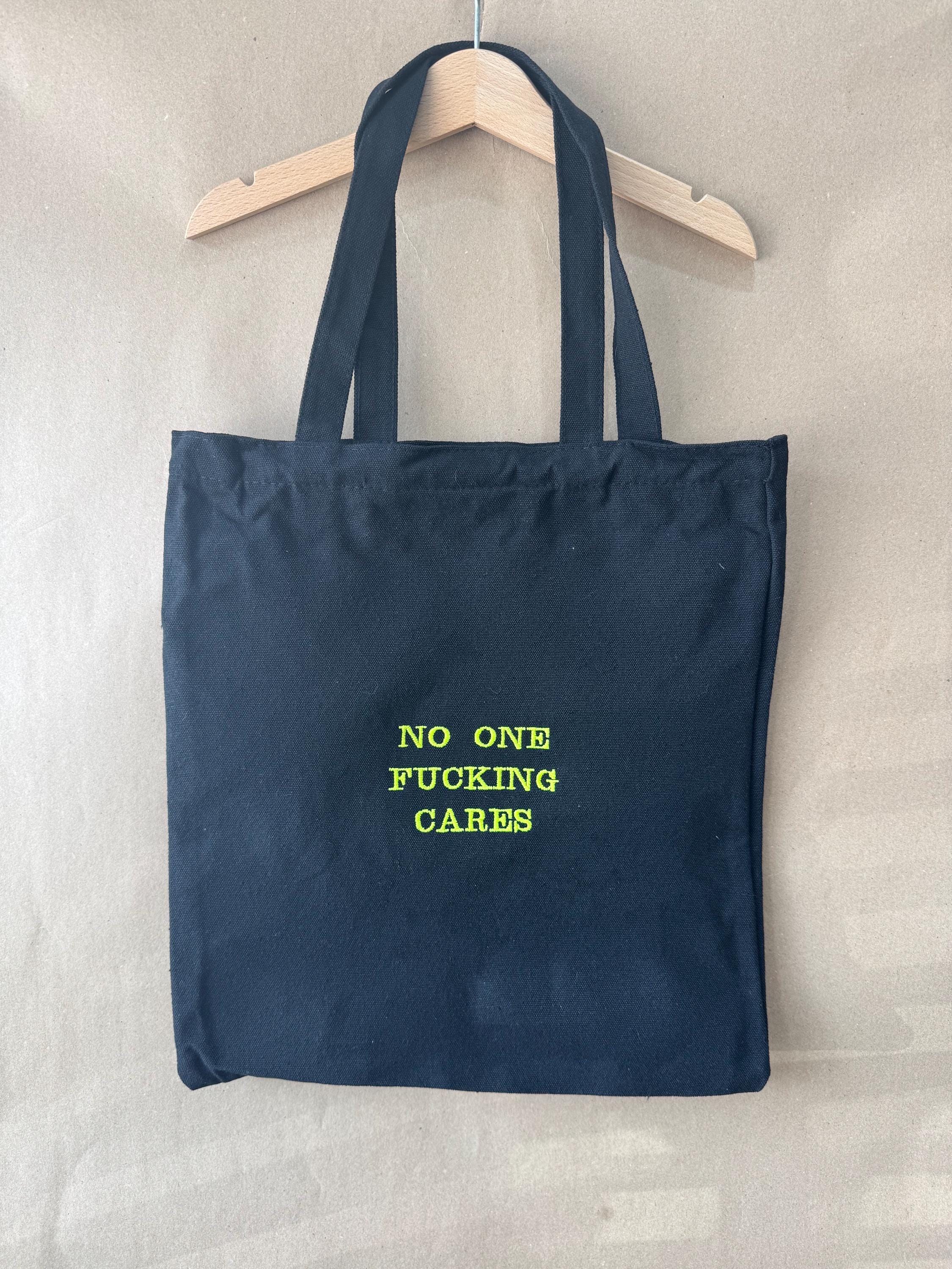 Black tote bag with ‘No one fucking cares’ embroidered in neon green