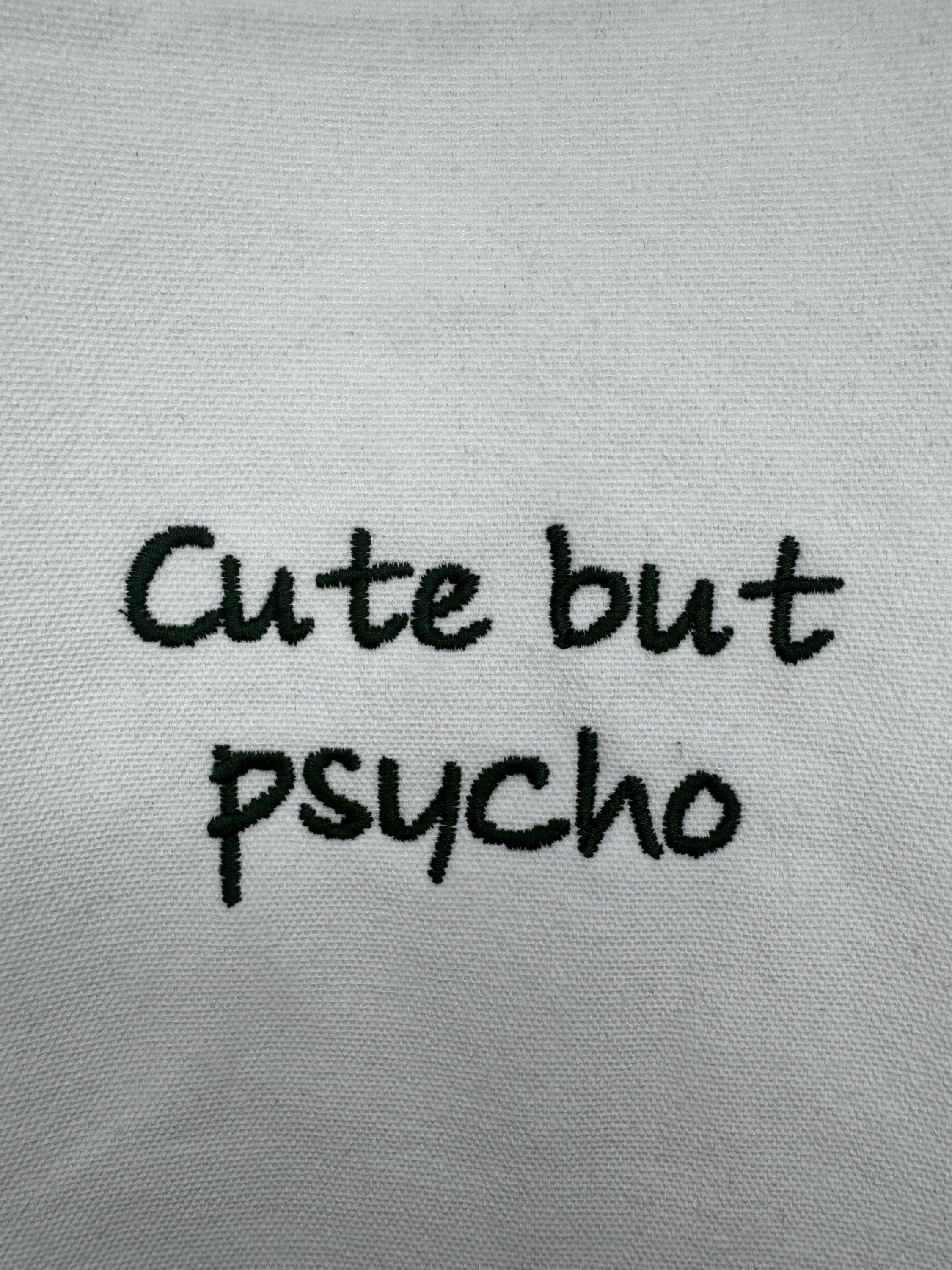 White tote bag with ‘cute but psycho’ embroidered in green.