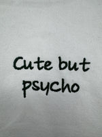 White tote bag with ‘cute but psycho’ embroidered in green.