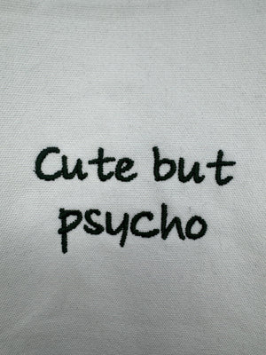 White tote bag with ‘cute but psycho’ embroidered in green.