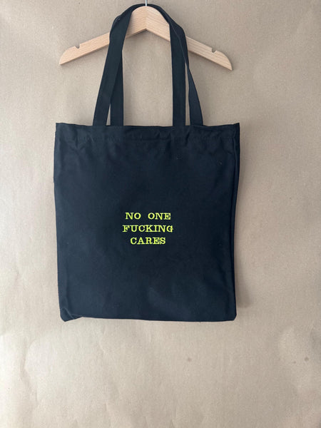 Black tote bag with ‘No one fucking cares’ embroidered in neon green