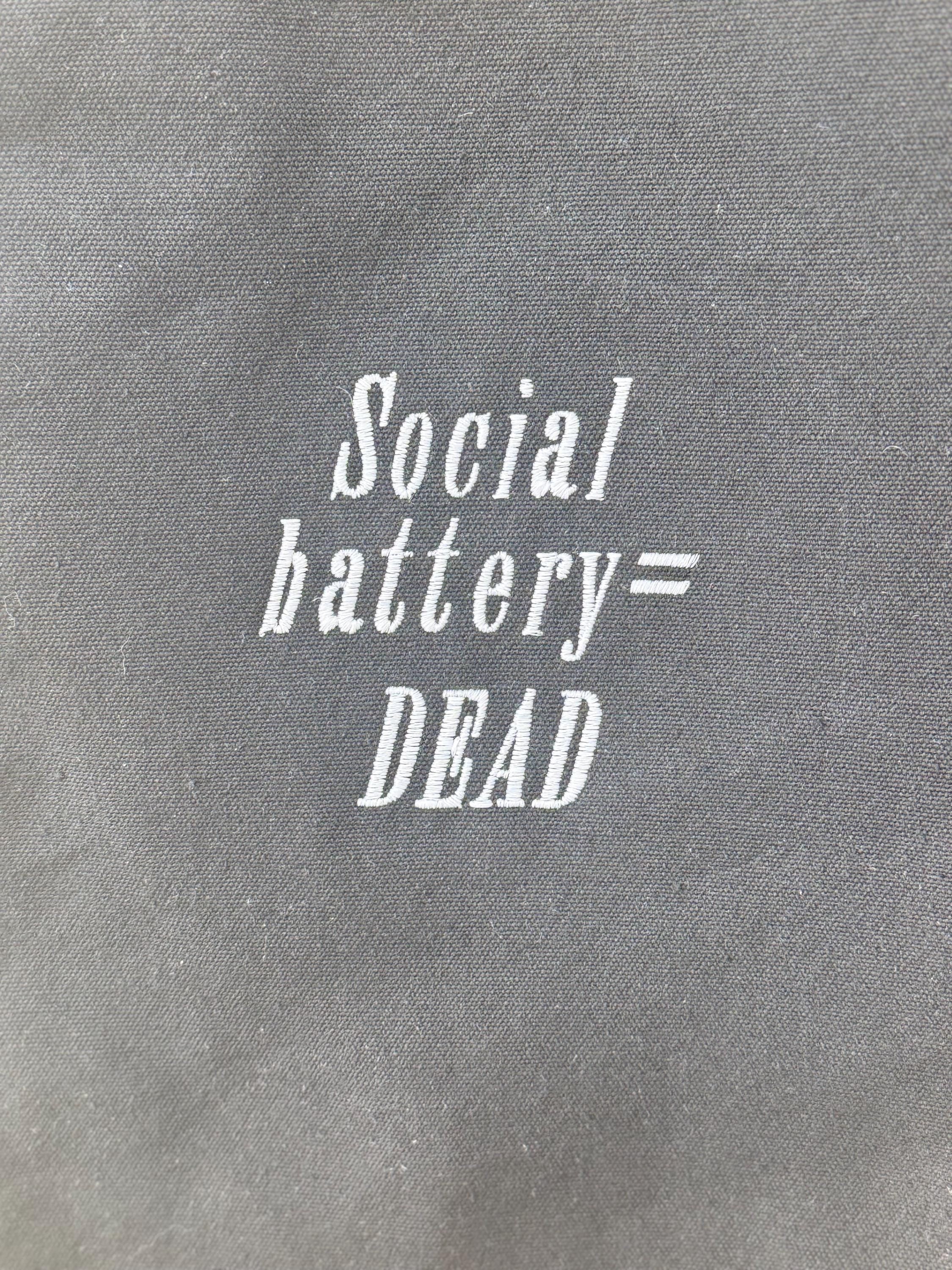 Black tote bag with ‘Social battery= DEAD’ embroidered in white.